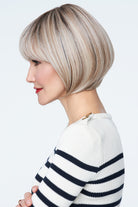 Profile of a woman with a blonde wig wearing a striped sweater on a white background