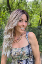 A woman with long blonde-highlighted hair wearing a camouflage-patterned tank top (Phillip by Rene of Paris in Melted Marshmallow R).