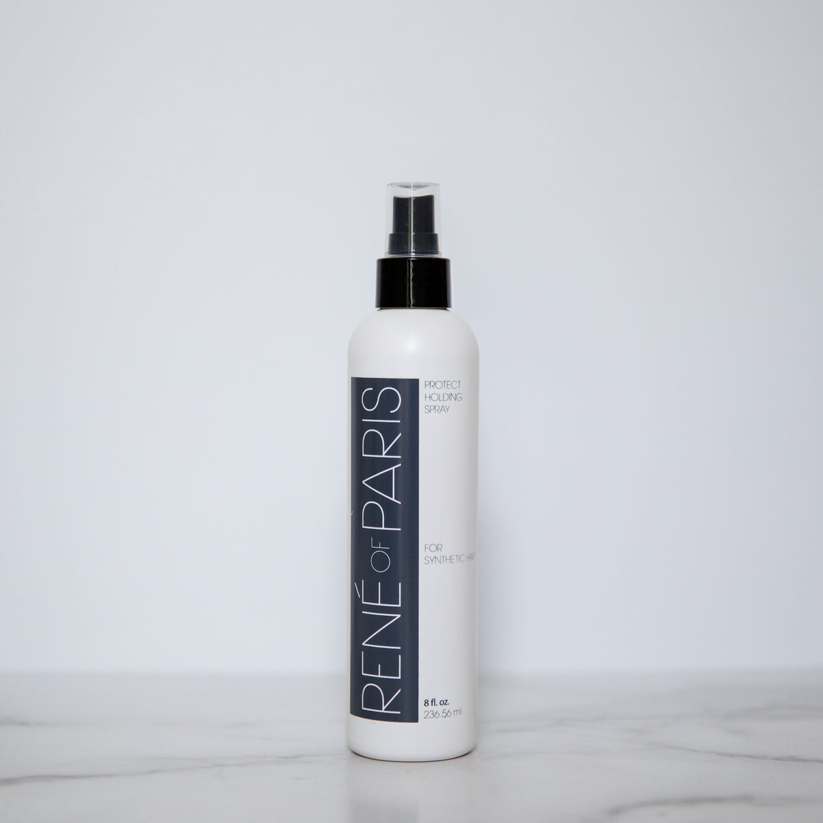 A white bottle of René de Paris Moist Locking Spray with a black spray nozzle, standing on a light marble surface against a plain light gray background.