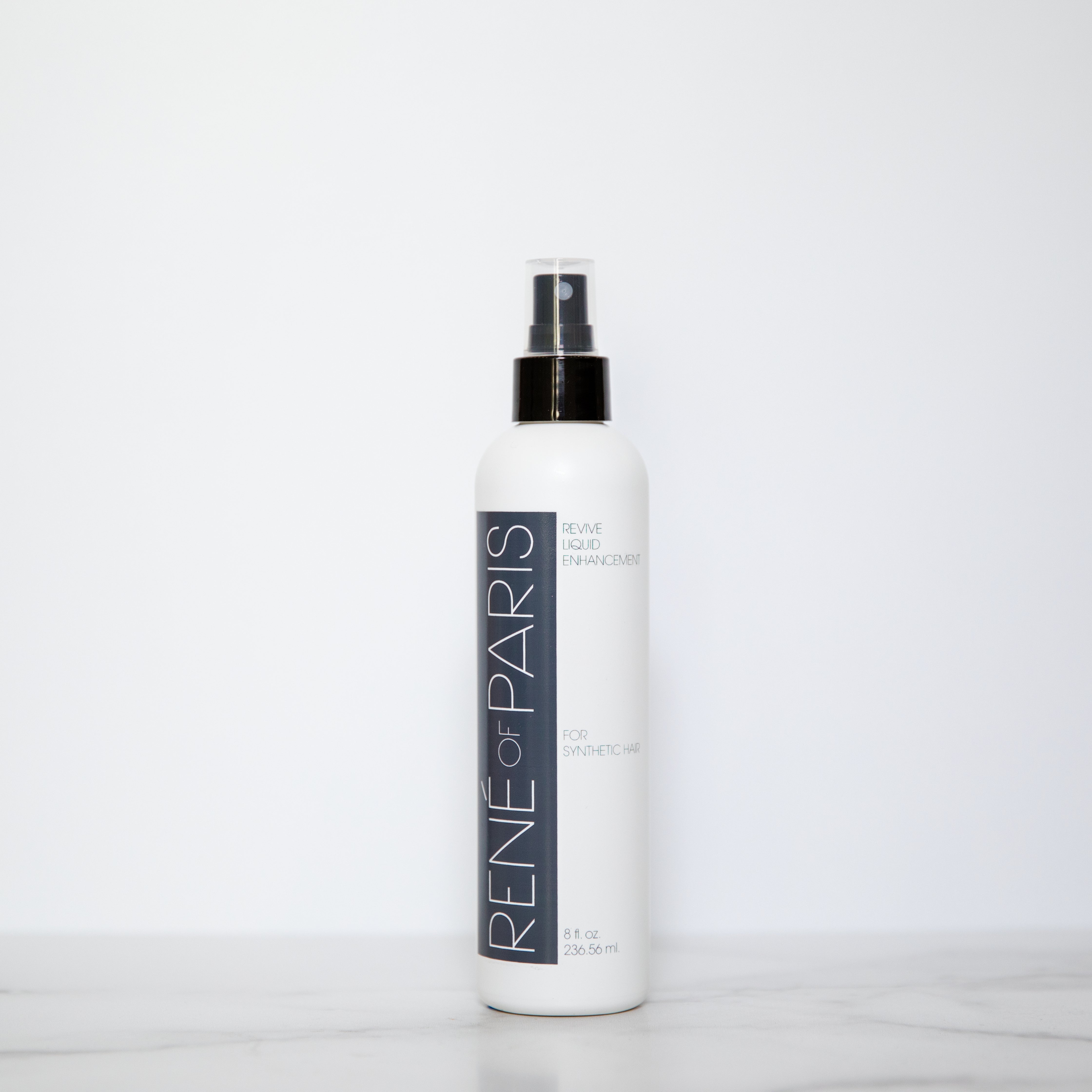 A white bottle of Rene-For-Paris Blue Blue Enhancer spray with a black pump and clear cap, standing on a light marble surface against a white background.