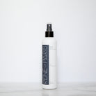 A white bottle of Rene-For-Paris Blue Blue Enhancer spray with a black pump and clear cap, standing on a light marble surface against a white background.