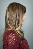 A woman with shoulder-length layered brown hair with blonde highlights and straight-cut bangs (wearing Revelry by Gabor in color Brown Blonde).