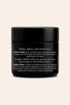 A black cosmetic jar with a matte black lid, featuring white text detailing directions for hair shaping and definition, set against a solid light beige background.