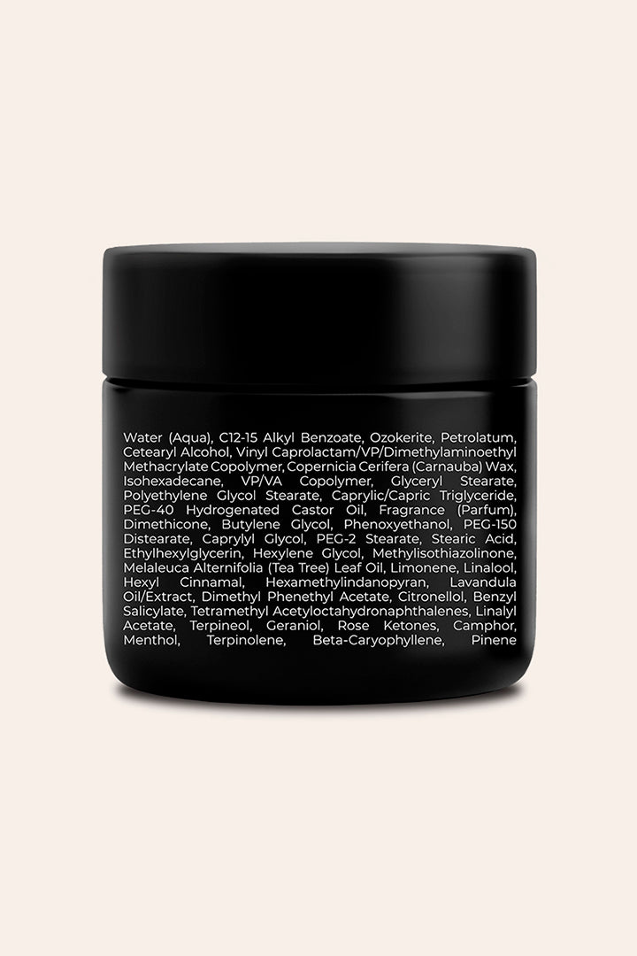 A small black cosmetic jar with a matte black lid and white text listing ingredients, centered on a light beige background.