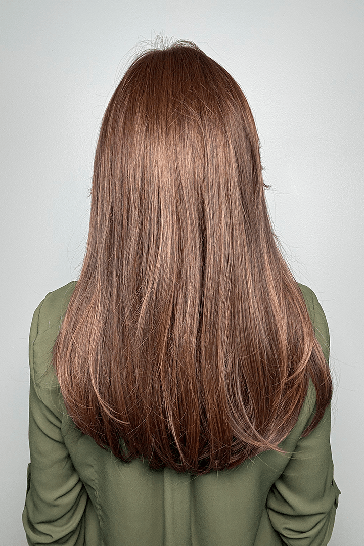 Woman wearing long layered wig with curtain bangs (Sleek Sophistication by Raquel Welch in color Copper Mahogany) back