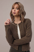 Woman in umber cardigan holding glasses, Snowy Wavez hairstyle.