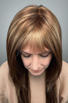 Woman wearing long brunette wig with bangs and highlights (Stevie by Amore in Honey Wheat) 