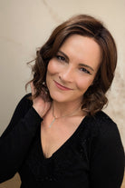 A woman with shoulder-length brown curly hair wearing a black long-sleeve top (Streep by Belle Tress in color Soft Amber Brown).