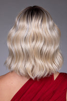 Back view of a blonde, wavy chin-length bob wig with dark roots and heat-friendly synthetic fibers.