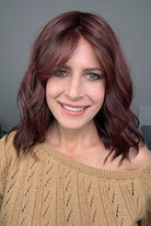 Woman wearing shoulder-length wavy wig with purple highlights (Smooth Wavez by Rene of Paris in color Plum Brown R)
