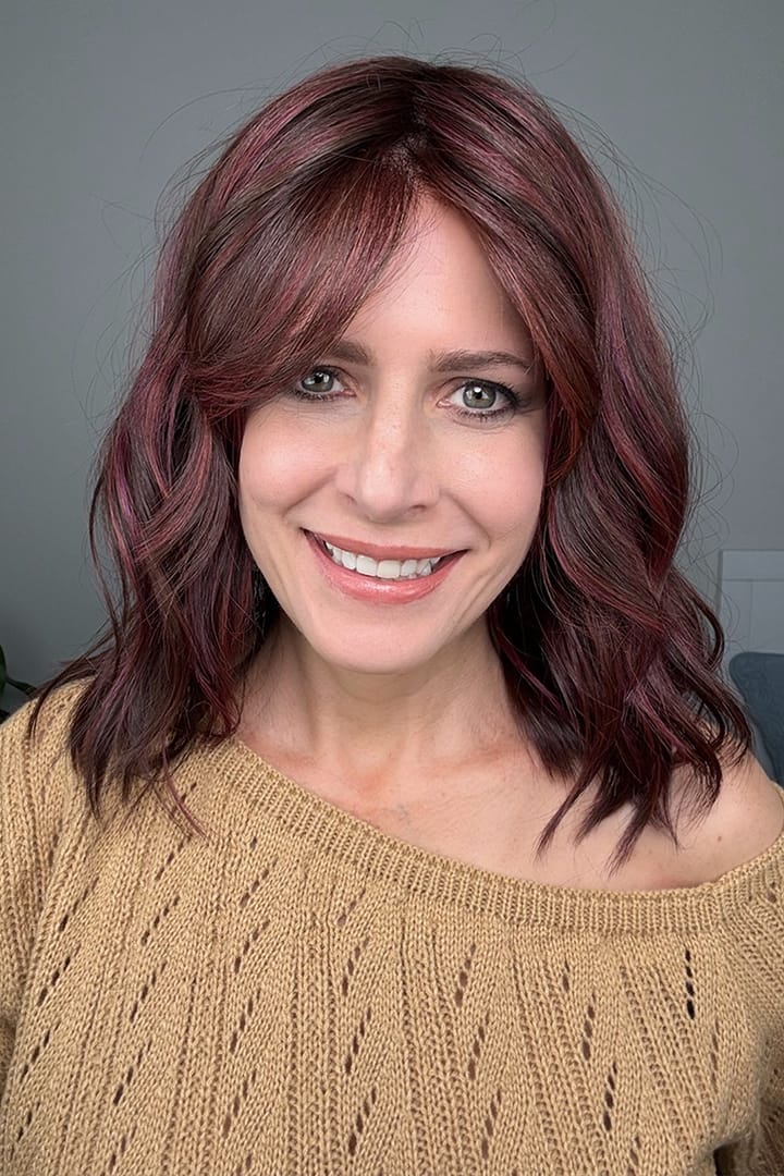 Woman wearing shoulder-length wavy wig with purple highlights (Smooth Wavez by Rene of Paris in color Plum Brown R)