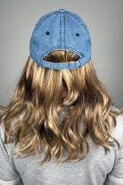 A woman with dark blonde hair wearing a blue denim baseball cap and a gray V-neck top (wearing Wavy Hat Denim in color 12/26H).
