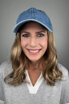 A woman with dark blonde hair wearing a blue denim baseball cap and a gray V-neck top (wearing Wavy Hat Denim in color 12/26H).