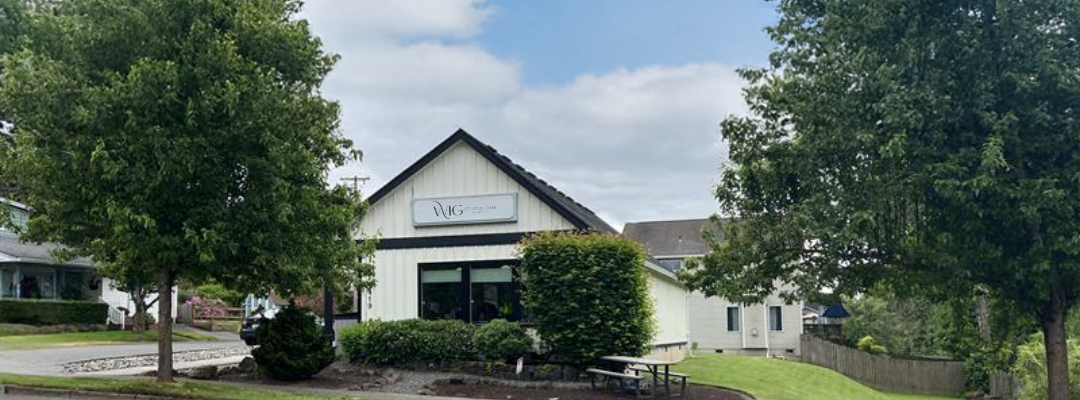 Small white building with a sloped roof surrounded by trees and a driveway.