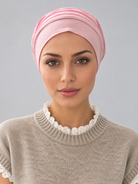 A woman wearing a rose melange turban-style head covering and a beige knit sweater with a white lace collar, photographed against a plain light gray studio background.