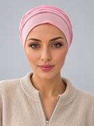 A woman wearing a rose melange turban-style cap, paired with a beige ribbed zip-up sweater, against a solid gray studio background. Front view
