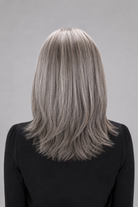 Woman wearing a Bespoke human hair wig by PUSH hair in color Sage, wearing a black blouse against a light grey background - back view