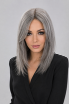 Woman wearing a Bespoke human hair wig by PUSH hair in color Sage, wearing a black blouse against a light grey background - front view