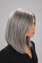 Woman wearing a Bespoke human hair wig by PUSH hair in color Sage, wearing a black blouse against a light grey background - right side view