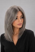 Woman wearing a Bespoke human hair wig by PUSH hair in color Sage, wearing a black blouse against a light grey background - front view