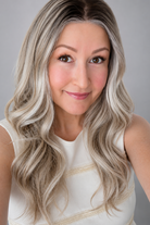 A woman wearing Bradley synthetic wig by PUSH in color champagne rooted with a cream sleeveless shirt against a grey background - front view