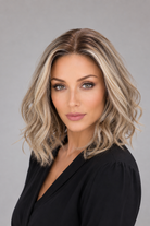 A woman wearing Brielle synthetic wig by PUSH in color Champagne Rooted - a shoulder-length, wavy blonde wig with darker roots, wearing a black top against a solid gray background - front view