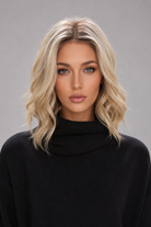 Woman wearing Brielle synthetic wig by PUSH in color golden champagne rooted with a black top against a light grey background. Front view.