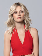 Demi Mono by Ellen Wille, a blonde wavy long bob wig with a lace front and monofilament top, worn by a woman in red.