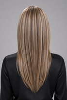 Woman wearing Evangeline heat friendly synthetic long wig in color cashmere bronde and a button down black blouse against a light grey background. Back view.