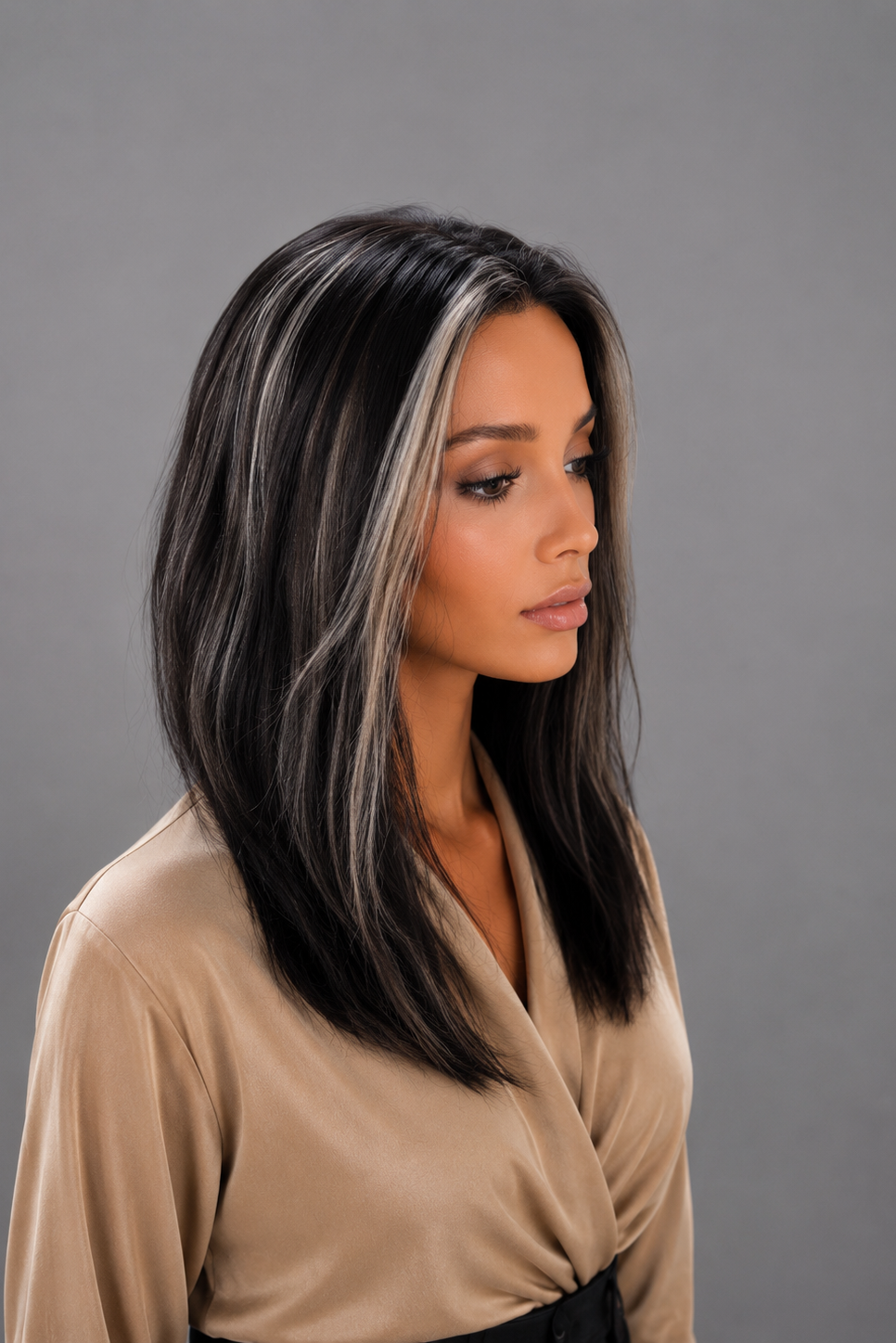 Woman wearing Gisele Human Hair Wig by PUSH in color Étoile Nocturne, a deep and rich off black base with chunky blonde highlights throughout and a tan blouse against a light grey background. Left side view.