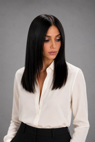 Woman wearing Jacey human hair wig by PUSH in color Noir with cream button down blouse and black pants with a light grey background. Front view. 