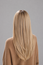 Woman wearing Remmie human hair wig by PUSH Hair in color champagne creme rooted and a tan sweater against a light grey background - back view