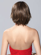 Back view of Tess Mono synthetic bob wig in a brown layered style with textured ends on a model in a red top.