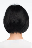 A woman wearing Abbey by Envy - A Human Hair and Heat Friendly Synthetic Blend wig in color black with a white sleeveless top against a white background. Back view.