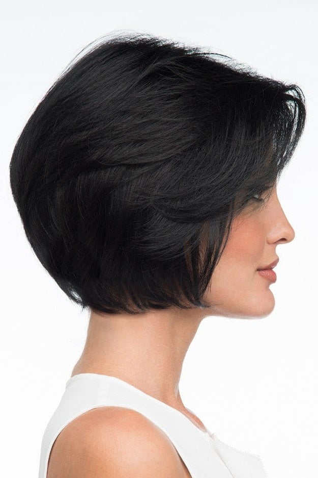A woman wearing Abbey by Envy - A Human Hair and Heat Friendly Synthetic Blend wig in color black with a white sleeveless top against a white background. Side view.